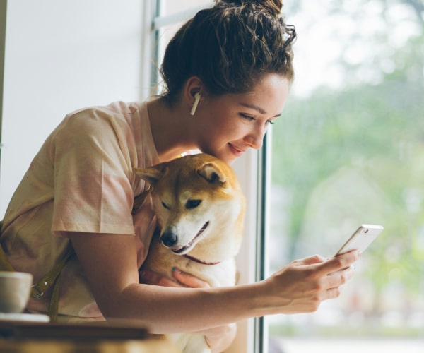 Simplify Your Pet’s Care—Right From Your Phone Girl looking in her phone while sitting with her pet dog hugging him
